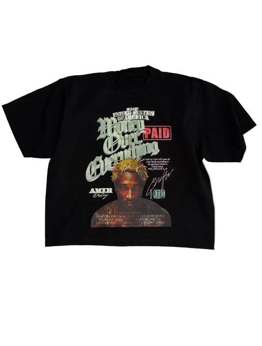 A black short-sleeve graphic t-shirt featuring a front print with the text 'Hang Your Money' in stylized green and white lettering, a red 'PAID' box, a portrait of a man, and a signature, laid flat on a white fabric background.